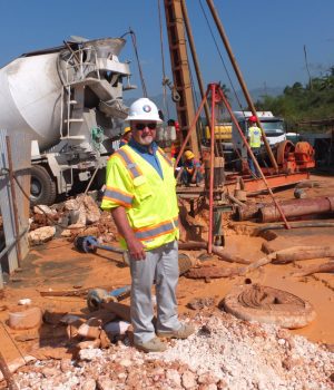 A man in yellow vest standing on dirt near construction equipment.