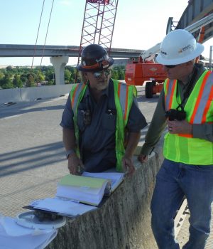 Two construction workers are standing on a bridge.