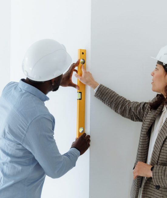 A man and woman are measuring the wall.