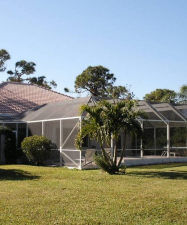 A large house with a screened in porch and lawn.